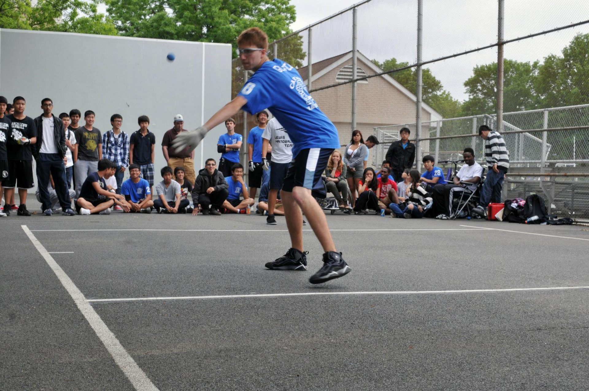 Young player serving with a crowd of teen players watching on a school handball court